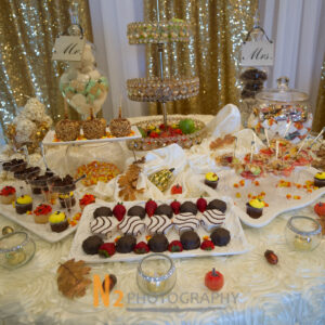 Wedding dessert table featuring chocolate covered strawberries, candy corn, caramel apples, cupcakes, and fruit.
