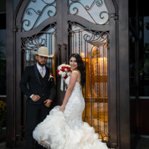 A bride holding a bouquet of flowers standing next to a groom wearing a cowboy hat at Alegria Gardens Reception Hall in Houston.