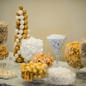 A beautiful dessert table with white and gold pretzels, candy, cake pops, and macarons at Alegria Gardens Reception Hall in Houston.