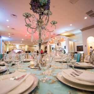 Close-up shot of a table featuring plates, cups, and a tall bouquet of purple and blue flowers at Alegria Gardens Reception Hall in Houston.