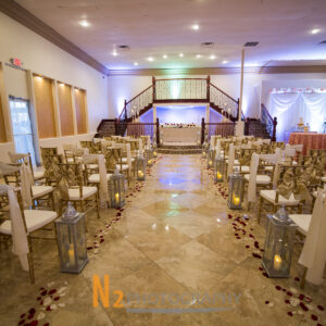 Wedding ceremony area with decorated tables, candles, and rose petals inside of Alegria Gardens Reception Hall in Houston.