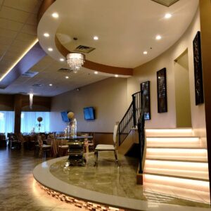 A picture of a table, two chairs, and a staircase on a raised platform inside of Alegria Gardens Reception Hall at Stacy in Houston.