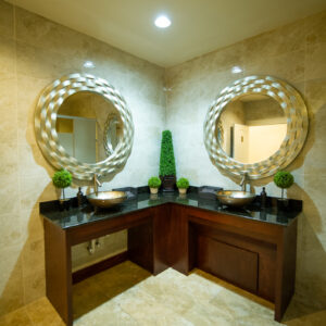 A picture taken inside of the bathroom at Alegria Gardens at 529 in Houston featuring two beautiful round mirrors, basin sinks, and five small shrubs.
