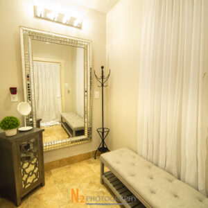 A picture taken inside of the changing room at Alegria Gardens at 529 in Houston featuring a large mirror, bright lights, and a soft bench.