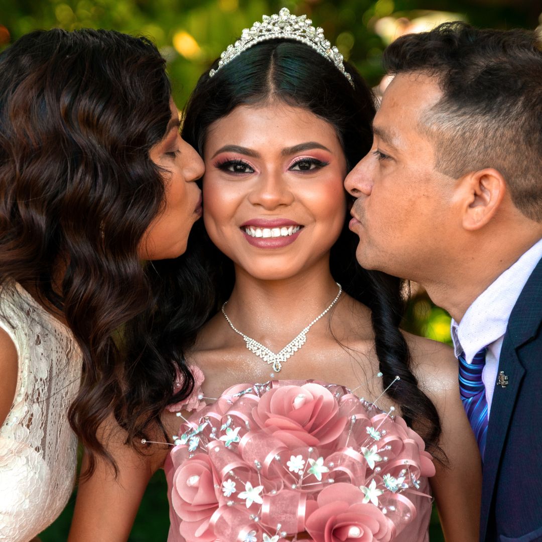girl being kissed on her cheek by her parents in a Quinceanera dress